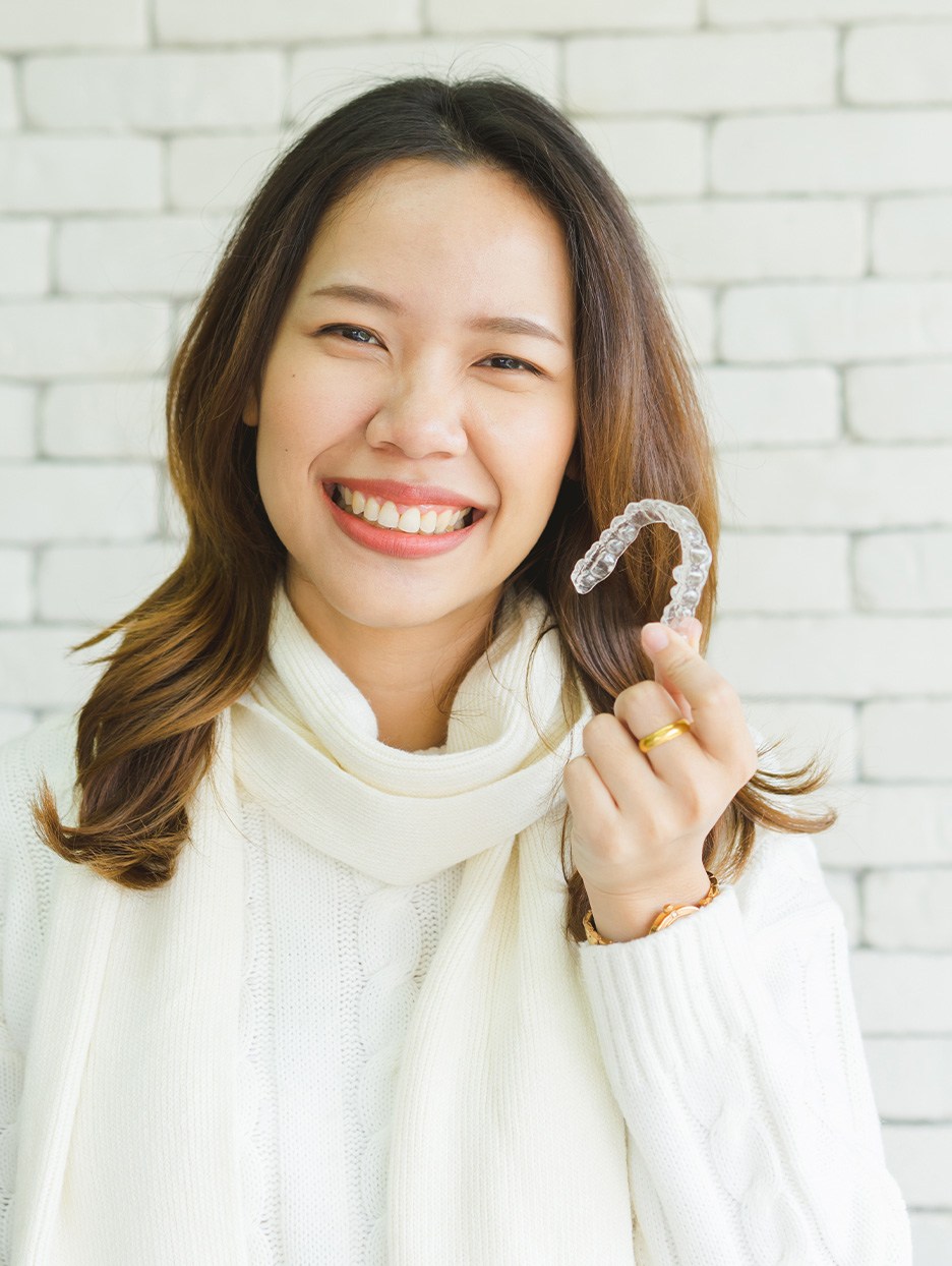 Woman in sweater holding Invisalign aligner