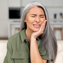 Woman in kitchen rubbing jaw due to tooth pain