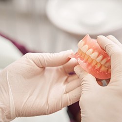 Gloved hands holding full dentures in Cary, NC