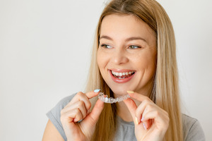 Young blonde woman holding an Invisalign aligner